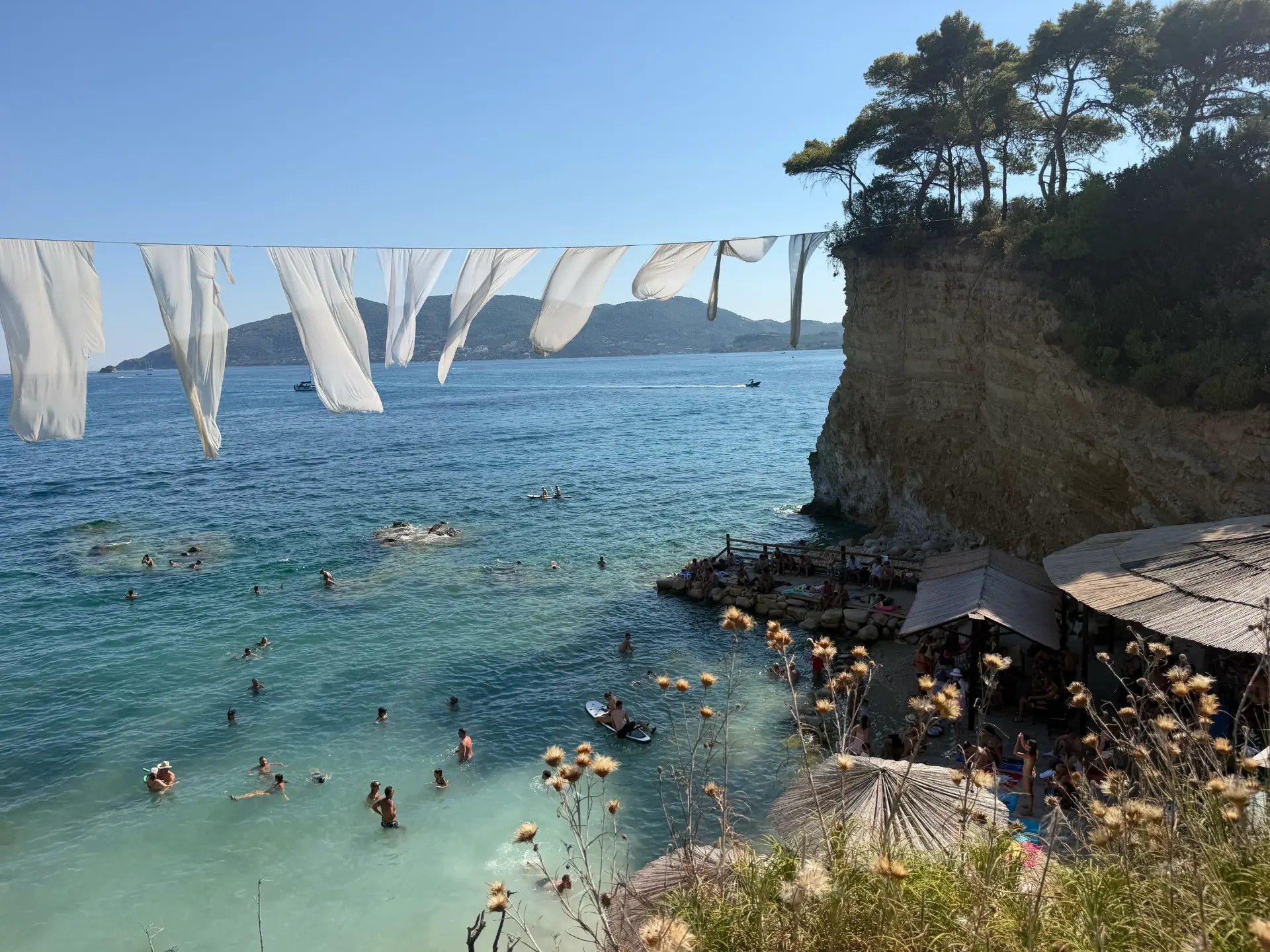 White fabric billowing on a line above a turquoise swimming cove by a rocky cliff